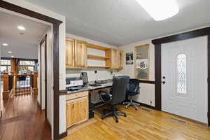 Office area featuring built in desk, light hardwood / wood-style floors, and a textured ceiling