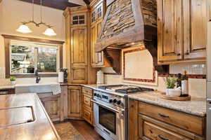 Kitchen with light stone counters, high end stove, tasteful backsplash, wall chimney range hood, and pendant lighting