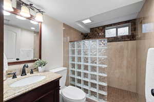 Bathroom featuring a tile shower, vanity, and toilet