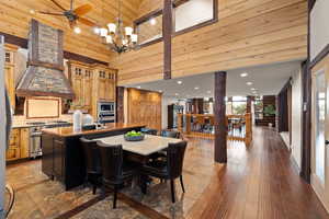 Dining area featuring ceiling fan with notable chandelier, high vaulted ceiling, and wood-type flooring