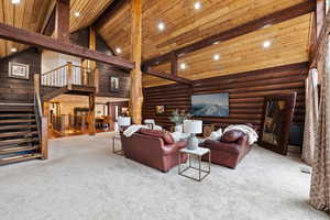 Living room featuring rustic walls, light carpet, high vaulted ceiling, and beam ceiling