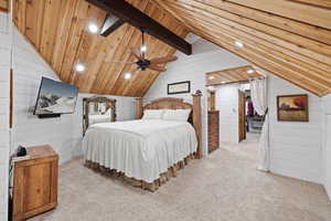 Carpeted bedroom featuring wooden walls and lofted ceiling with beams