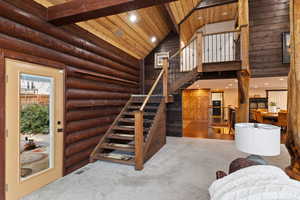 Stairs with log walls, high vaulted ceiling, beam ceiling, and wood ceiling