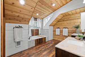 Bathroom featuring a bathtub, wood walls, lofted ceiling, wooden ceiling, and vanity