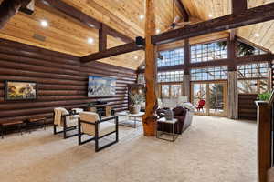 Living room featuring rustic walls, high vaulted ceiling, beam ceiling, ceiling fan, and light carpet