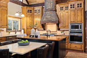 Kitchen with premium range hood, stainless steel appliances, a center island with sink, an inviting chandelier, and a kitchen breakfast bar