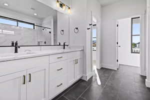 Bathroom featuring a healthy amount of sunlight, tile patterned floors, a shower with door, and dual bowl vanity