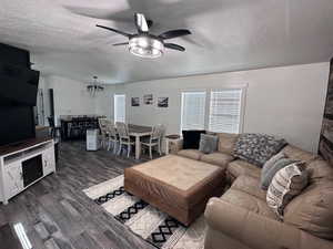 Living room with a textured ceiling, ceiling fan, and dark wood-type flooring