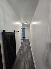 Hall featuring dark wood-type flooring, a textured ceiling, and a barn door