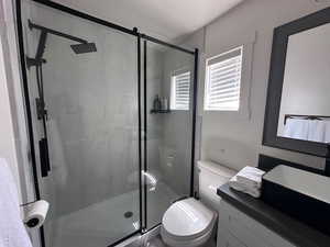 Bathroom featuring a shower with shower door, vanity, and toilet