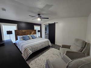 Bedroom featuring multiple windows, ceiling fan, lofted ceiling, and a barn door