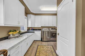 Kitchen with white cabinetry, ornamental molding, light stone counters, light hardwood / wood-style flooring, and independent washer and dryer