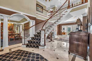 Interior space with light tile patterned flooring, decorative columns, crown molding, and a chandelier