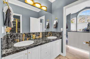 Bathroom featuring crown molding, double vanity, hardwood / wood-style floors, decorative backsplash, and vaulted ceiling