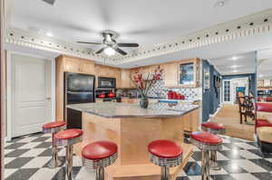 Kitchen featuring black appliances, light brown cabinets, backsplash, crown molding, and a center island