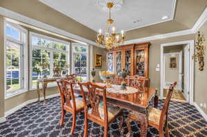 Carpeted dining room featuring plenty of natural light, a chandelier, and ornamental molding