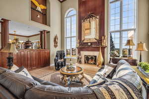 Living room with light hardwood / wood-style floors, ornate columns, a towering ceiling, a tile fireplace, and ornamental molding