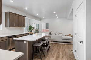 Kitchen featuring stainless steel dishwasher, a center island, dark brown cabinetry, light hardwood / wood-style flooring, and a kitchen breakfast bar