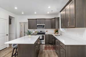 Kitchen with dark brown cabinets, a center island, stainless steel appliances, wood-type flooring, and sink