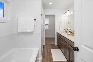 Bathroom with dual bowl vanity, a bath, wood-type flooring, and a healthy amount of sunlight