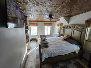 Bedroom with light tile patterned floors, ceiling fan, and crown molding