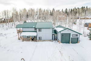 Snow covered back of property with an outdoor structure and a garage