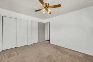 Unfurnished bedroom with two closets, light carpet, and ceiling fan