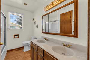 Full bathroom featuring shower / bath combination with glass door, toilet, wood-type flooring, and double vanity