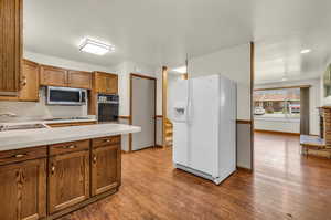 Kitchen with gas cooktop, sink, oven, wood-type flooring, and white fridge with ice dispenser