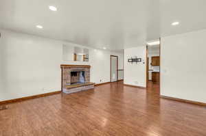 Unfurnished living room featuring wood-type flooring and a brick fireplace