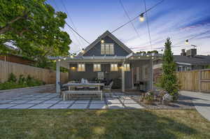 Back house at dusk featuring central air condition unit, a patio, and a lawn