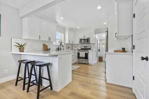 Kitchen with light hardwood / wood-style floors, appliances with stainless steel finishes, tasteful backsplash, and white cabinets