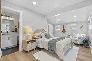 Bedroom featuring light hardwood / wood-style floors, vaulted ceiling with beams, ensuite bath, and sink