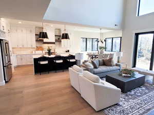 Living room featuring an inviting chandelier, light wood-type flooring, a high ceiling, and plenty of natural light