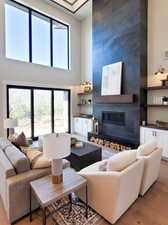 Living room featuring light wood-type flooring, a towering ceiling, and a large fireplace