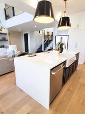 Kitchen with light wood-type flooring, dishwasher, a kitchen island with sink, sink, and hanging light fixtures