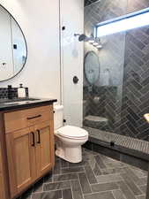 Bathroom with a tile shower, tile patterned floors, vanity, and toilet