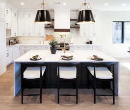 Kitchen with a center island with sink, light hardwood / wood-style floors, a kitchen breakfast bar, and white cabinetry