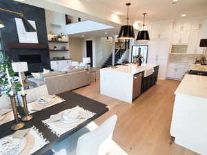 Kitchen featuring white cabinetry, an island with sink, a fireplace, dishwasher, and decorative light fixtures