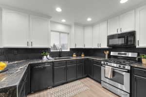 Kitchen with sink, light hardwood / wood-style flooring, white cabinetry, backsplash, and black appliances