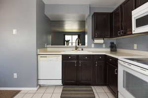 Kitchen featuring dark brown cabinets, sink, white appliances, and light tile patterned floors