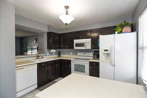 Kitchen featuring white appliances, light tile patterned floors, kitchen peninsula, dark brown cabinetry, and sink