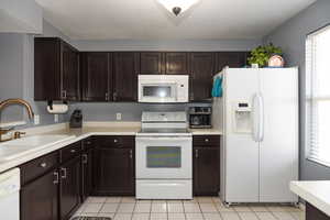 Kitchen featuring light tile patterned floors, dark brown cabinetry, white appliances, and sink