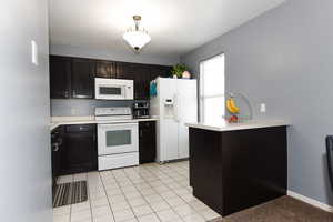 Kitchen featuring light tile patterned flooring, kitchen peninsula, and white appliances