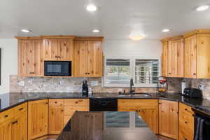 Kitchen featuring dark stone countertops, sink, decorative backsplash, and black appliances