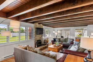 Living room featuring a fireplace, beamed ceiling, baseboard heating, and a healthy amount of sunlight