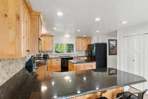 Kitchen featuring range with electric cooktop, light brown cabinets, kitchen peninsula, decorative backsplash, and black refrigerator with ice dispenser