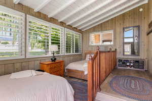 Bedroom with vaulted ceiling with beams, multiple windows, wooden walls, and wood-type flooring