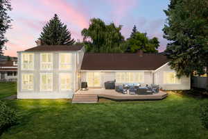 Back house at dusk with a yard, outdoor lounge area, and a wooden deck