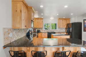 Kitchen with tasteful backsplash, range with electric cooktop, black fridge with ice dispenser, and kitchen peninsula